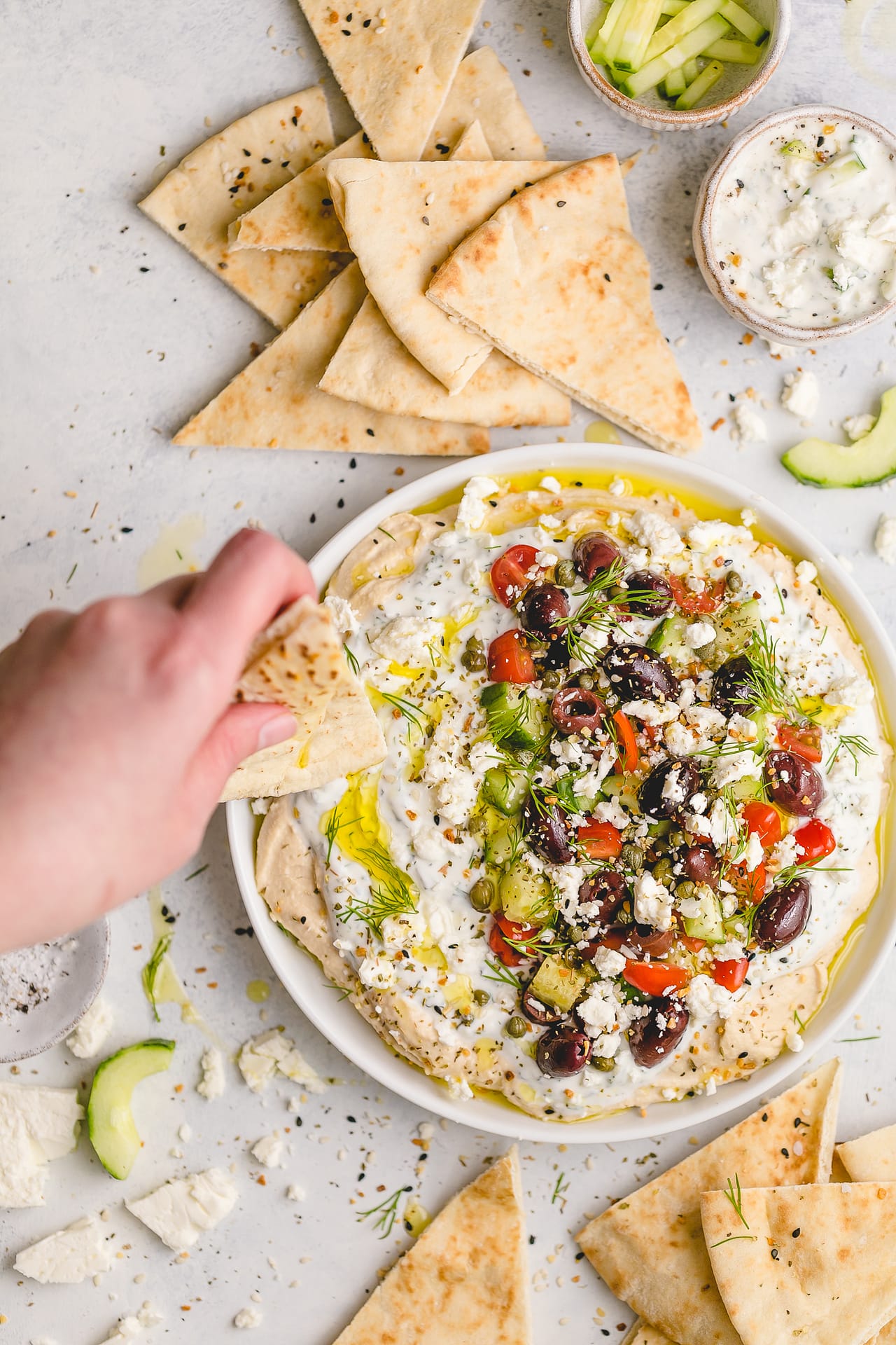 Salsa griega con hummus y tzatziki (134 calorías): ¡un aperitivo lleno de sabor que puedes disfrutar! Una capa de garbanzos deliciosamente suaves, una capa de tzatziki con hierbas frescas y aderezos como queso feta, pepinos frescos picados, tomates dulces, alcaparras saladas y aceitunas.